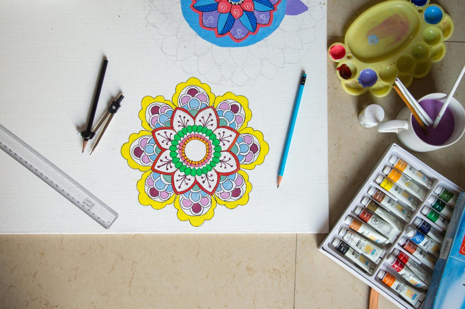 Vibrant mandala drawing with pencils, paint, and tools arranged neatly on a workspace.